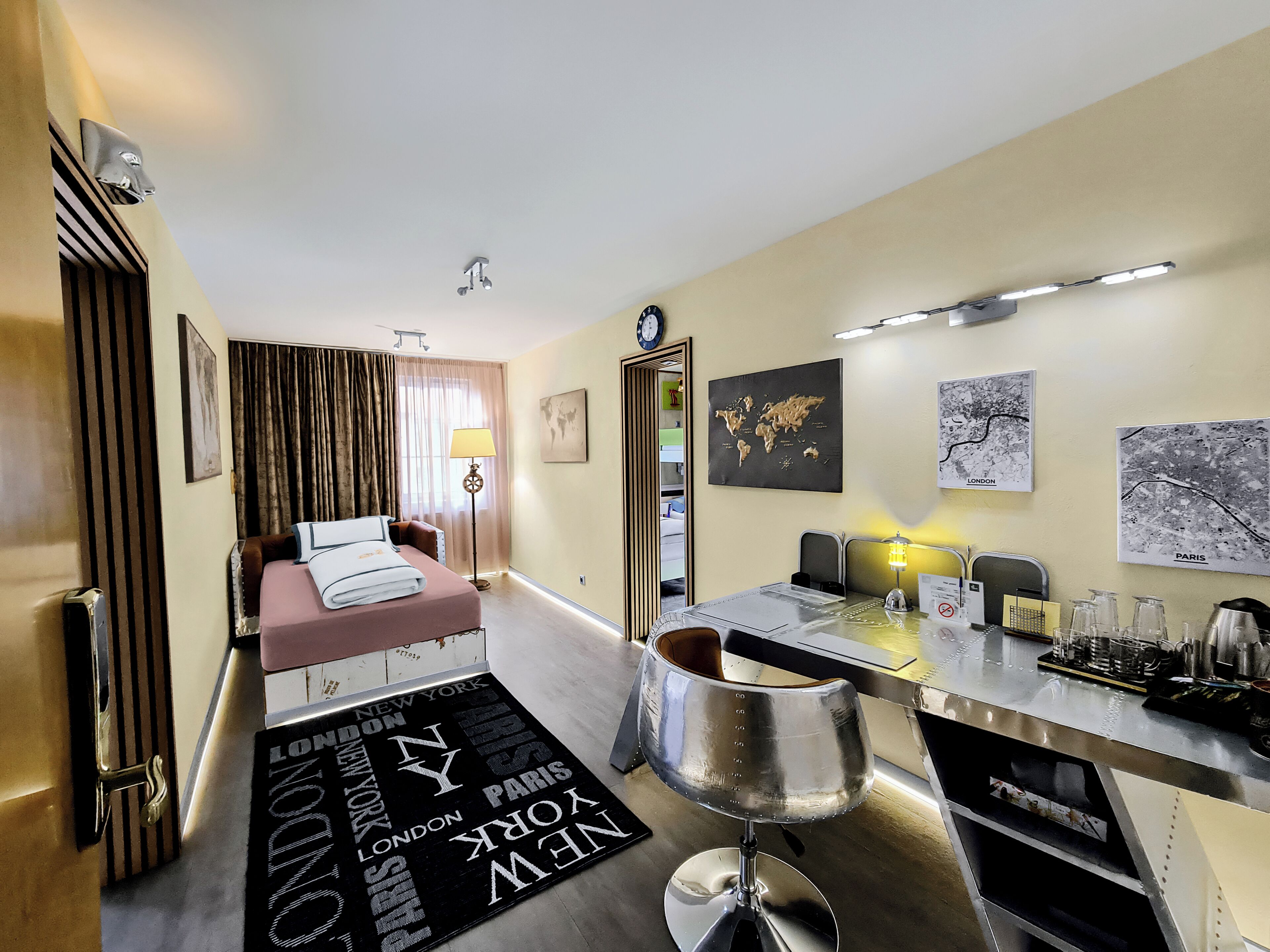 A hotel room with a bed, a desk, a chair, a map of the world, and a globe.