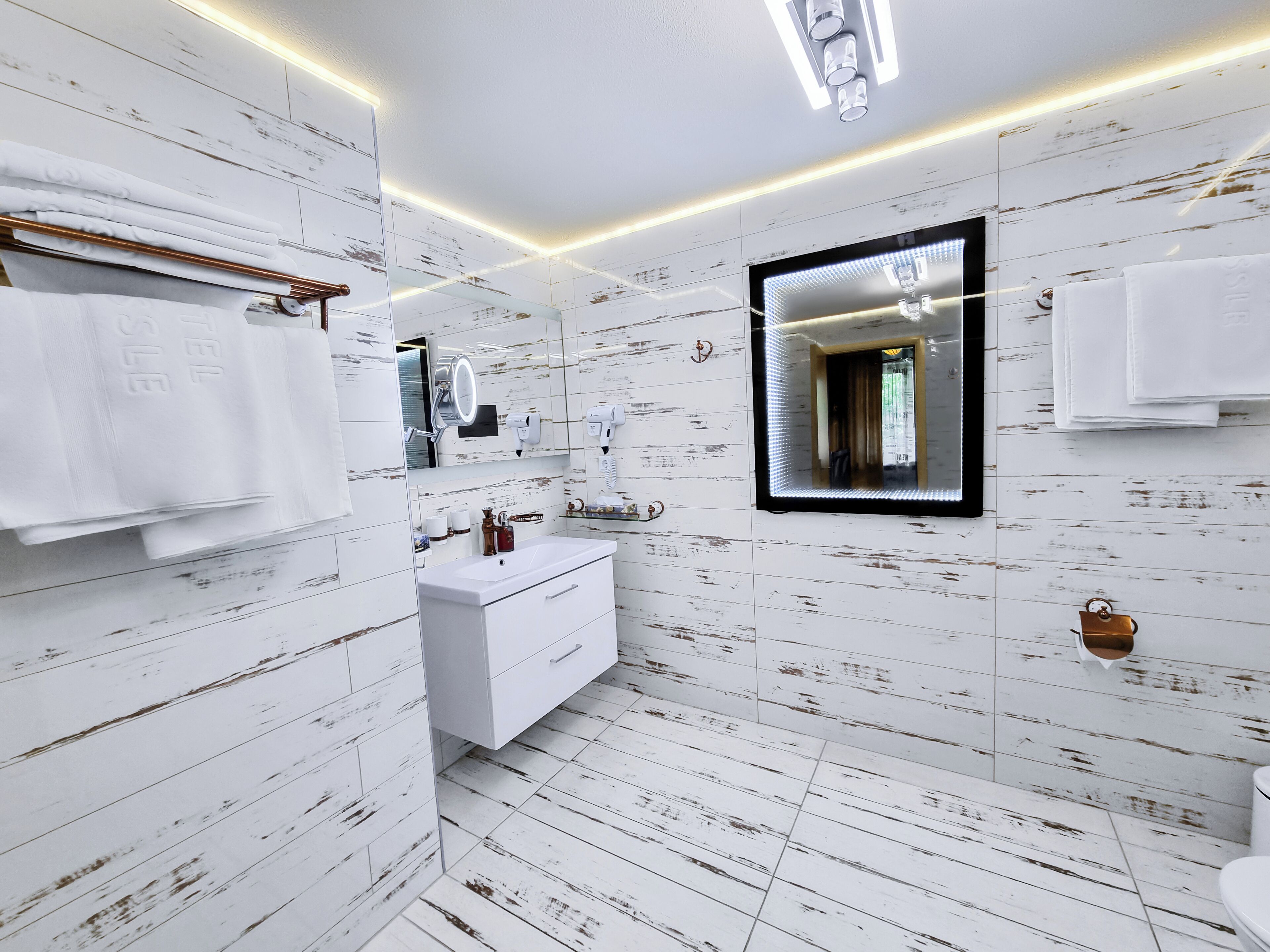 A modern bathroom with white wooden paneling, a white sink, and a large mirror.