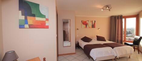 Habitación de hotel con dos camas, un escritorio con lámpara, una silla y obras de arte en las paredes.