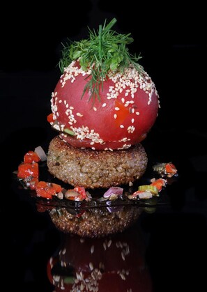 A burger with a tomato slice on top, garnished with sesame seeds and a sprig of green herb. - Hôtel Logis Carasol (Elne)