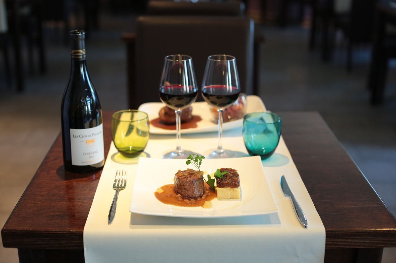 A dining table with a bottle of wine, two wine glasses, a plate with food, and cutlery.