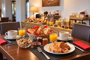 A breakfast setting with croissants, orange juice, and coffee on a wooden table. - Hôtel Logis Carasol (Elne)