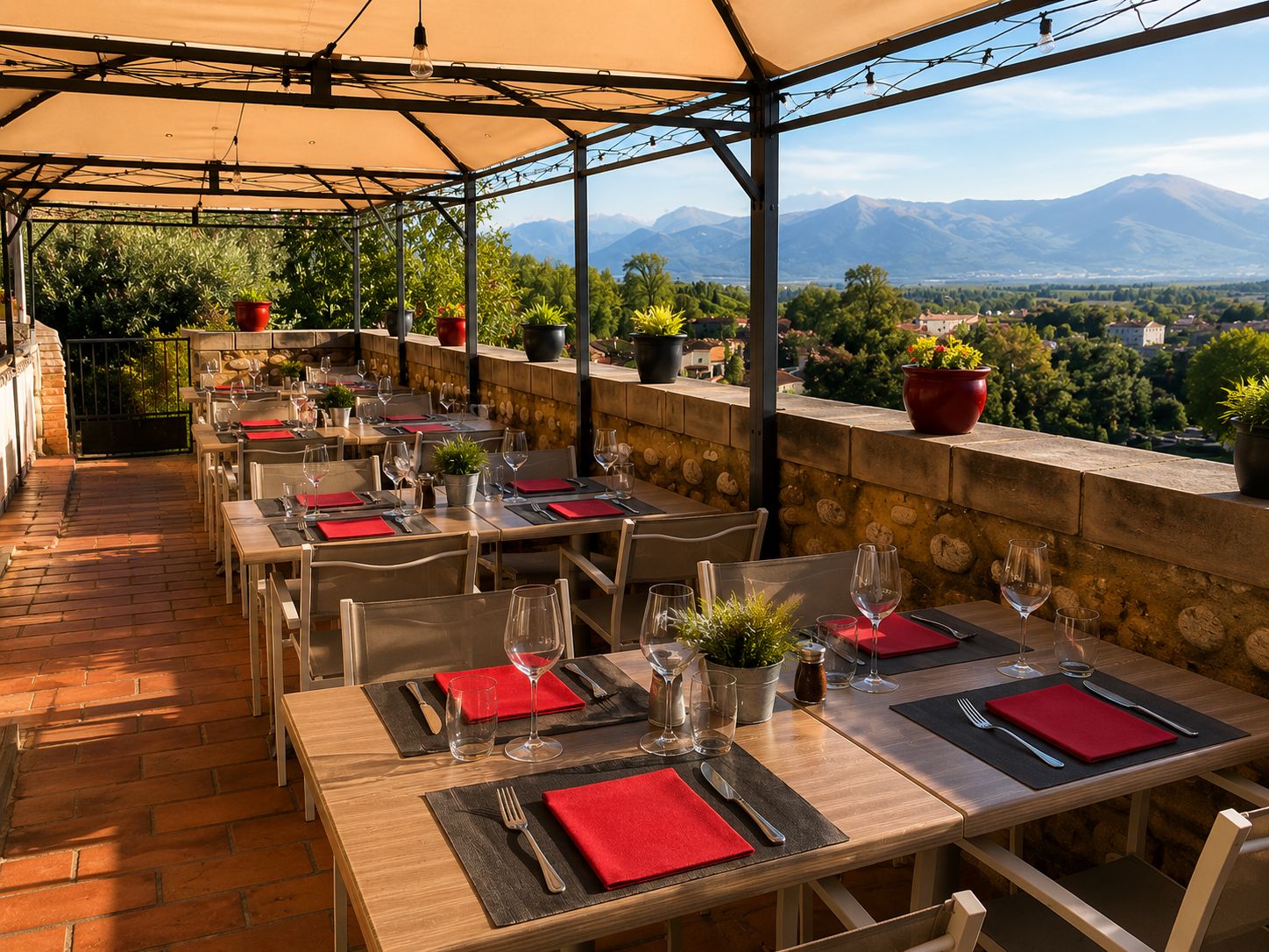 An outdoor restaurant with tables set for dining, potted plants, and a view of mountains.