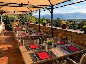 An outdoor restaurant with tables set for dining, potted plants, and a view of mountains. - Hôtel Logis Carasol (Elne)