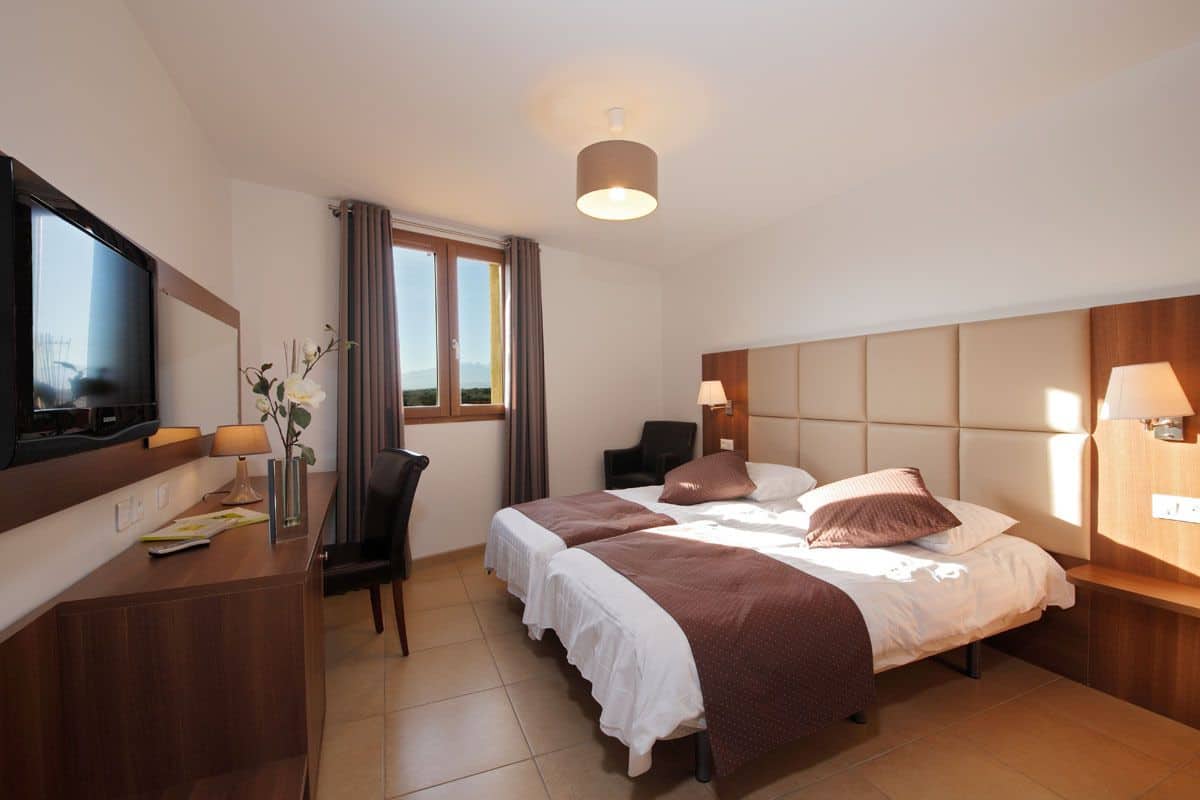 A hotel room with a bed, a desk, a television, and a window with curtains.