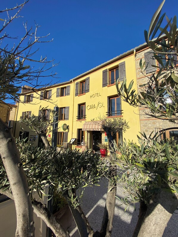 A yellow building with 'HOTEL' and 'RESTAURANT' signage, featuring a stone facade and multiple windows. - Hôtel Logis Carasol (Elne)