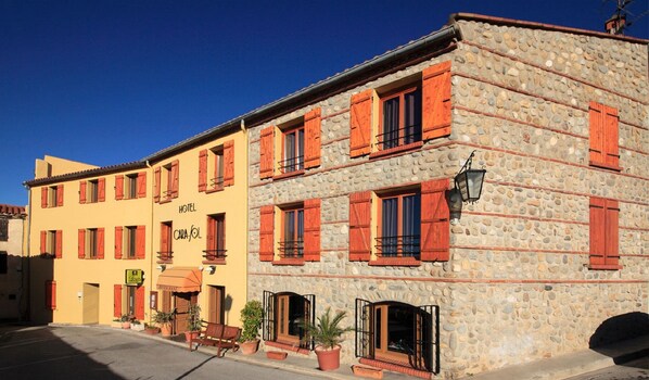 A hotel with a stone facade, multiple windows with red shutters, and a sign indicating it is a hotel named "CARA-COL". - Hôtel Logis Carasol (Elne)