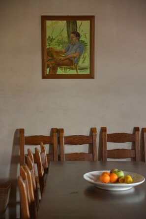 Una mesa de comedor con un plato de fruta, sillas de madera y un cuadro en la pared.