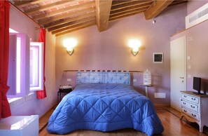 Un dormitorio con una colcha azul acolchada, techo de madera, cómoda blanca y mesita de noche con lámpara.