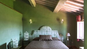 Quarto com uma cama grande, paredes verdes e teto de madeira. Há duas mesas de cabeceira com luminárias e um castiçal decorativo na parede.