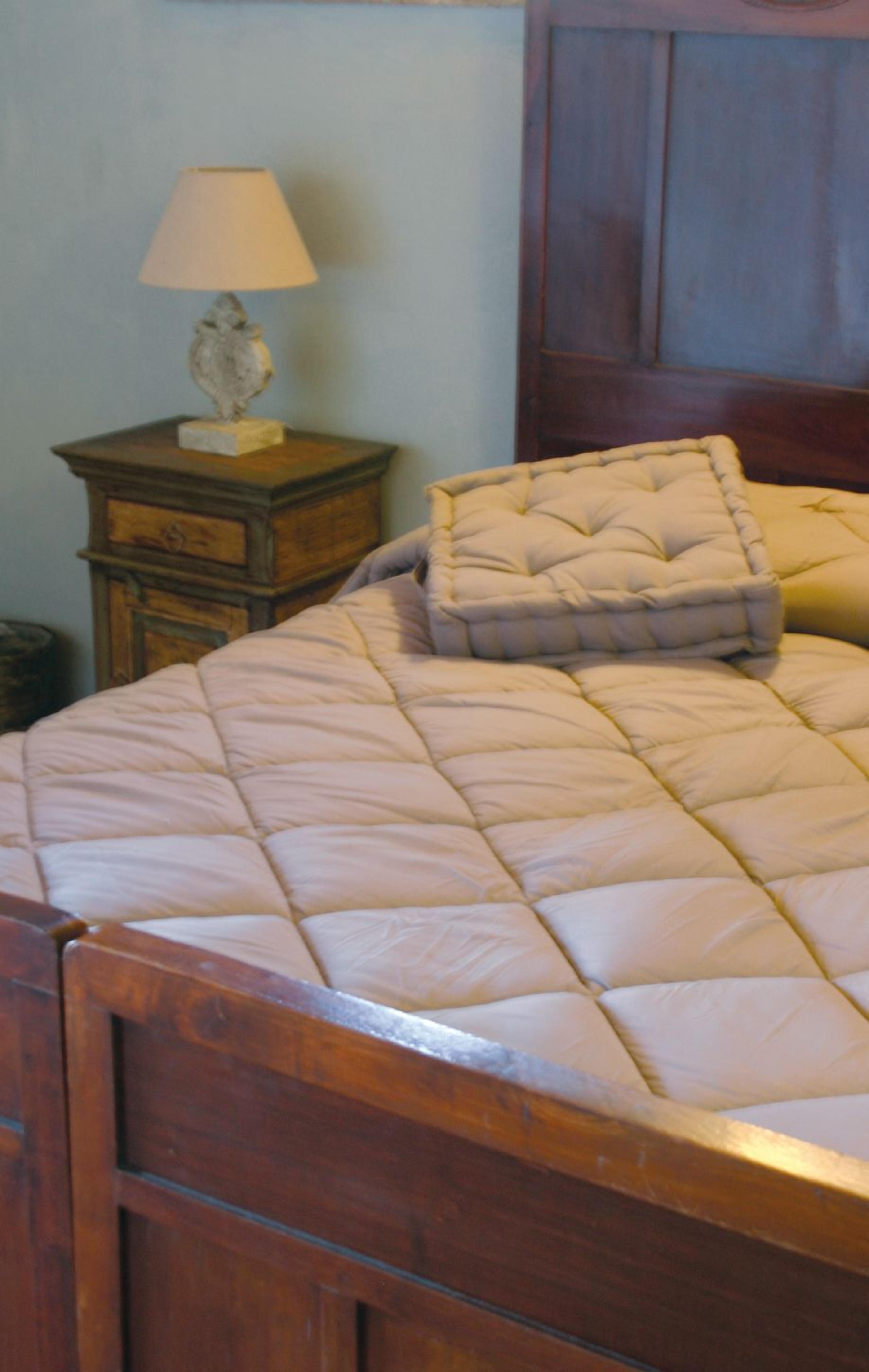 A bed with a quilted headboard and a matching pillow, a wooden nightstand with a lamp, and a wooden cabinet.