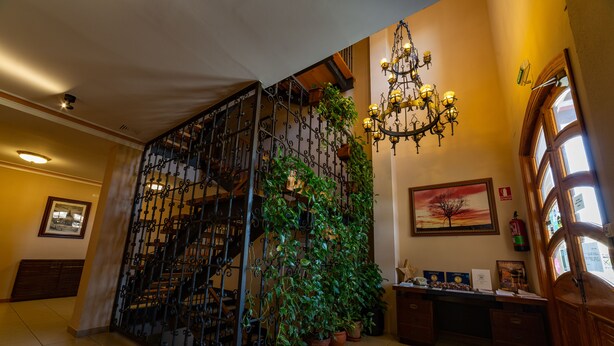 Un escalier orné d’une rampe en fer forgé, des plantes en pot, un lustre et un bureau avec des papiers et des récompenses.