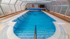 Une piscine intérieure avec des parois en verre transparent, un sol carrelé et un plongeoir central.