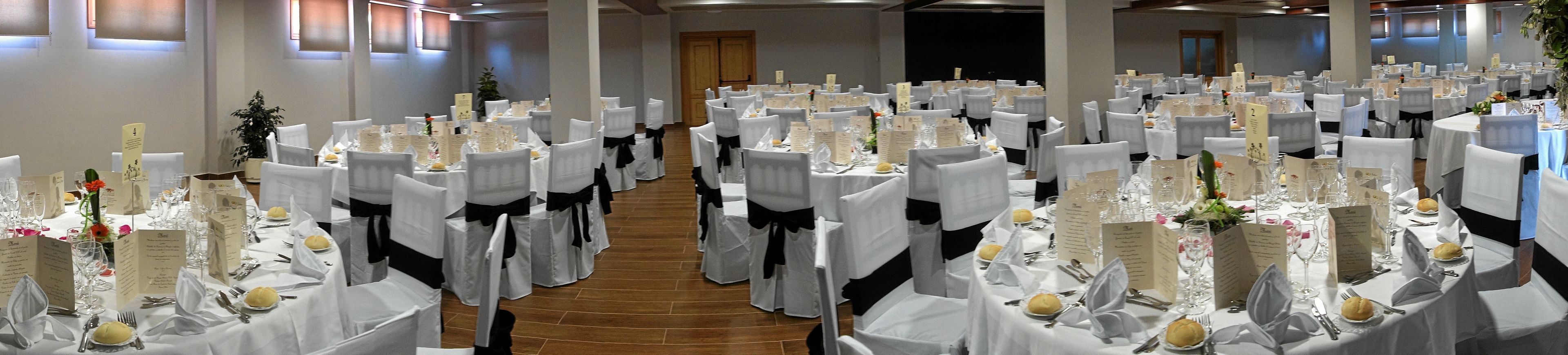 Un salón de banquetes con mesas redondas dispuestas para un evento formal, cada una con manteles blancos, fajos negros y menús.