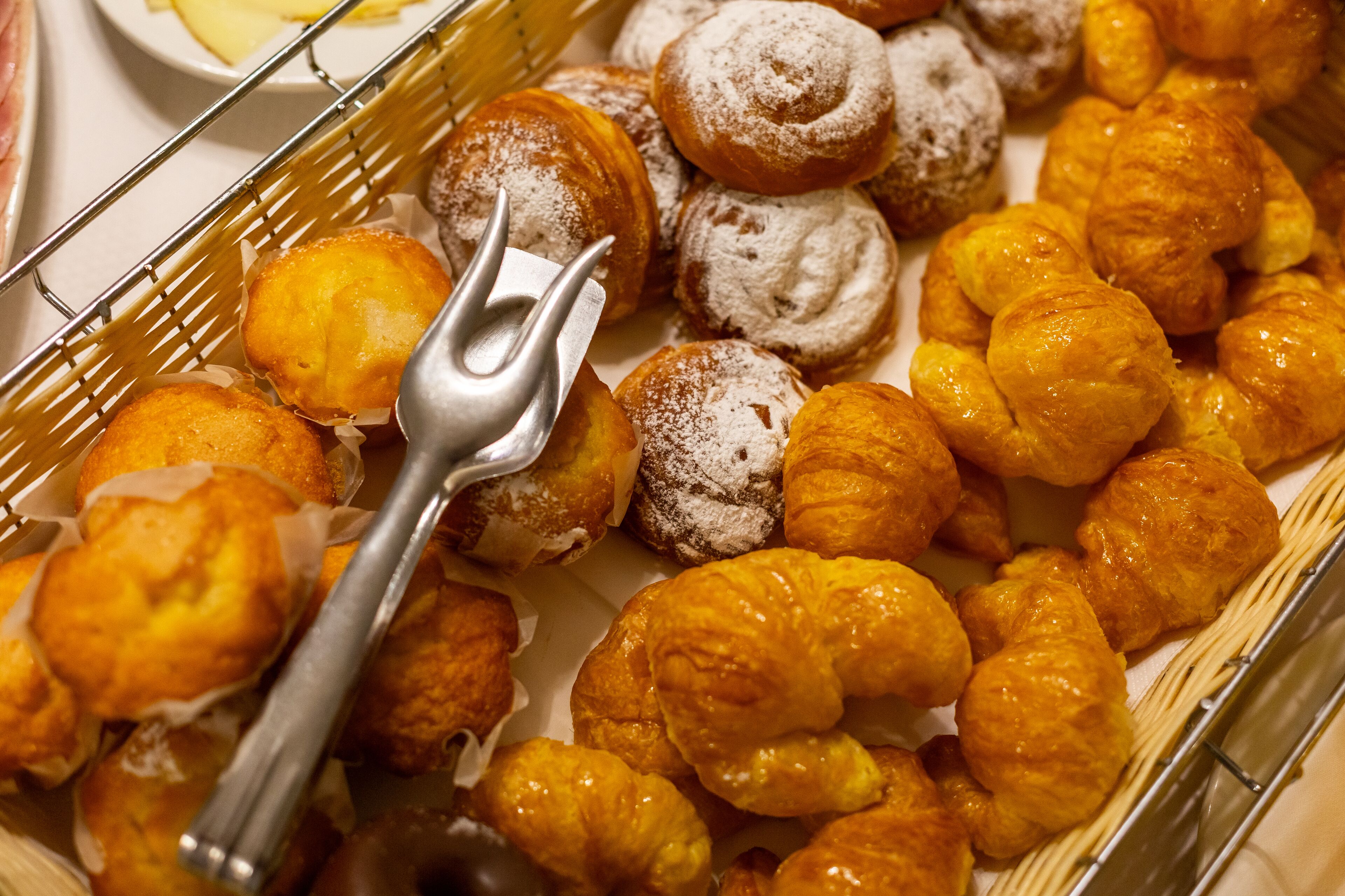 Una selección de pasteles en una cesta, entre ellos croissants y rosquillas espolvoreadas.