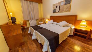 Una habitación de hotel con una cama de madera, un escritorio con computadora, una silla y una lámpara.