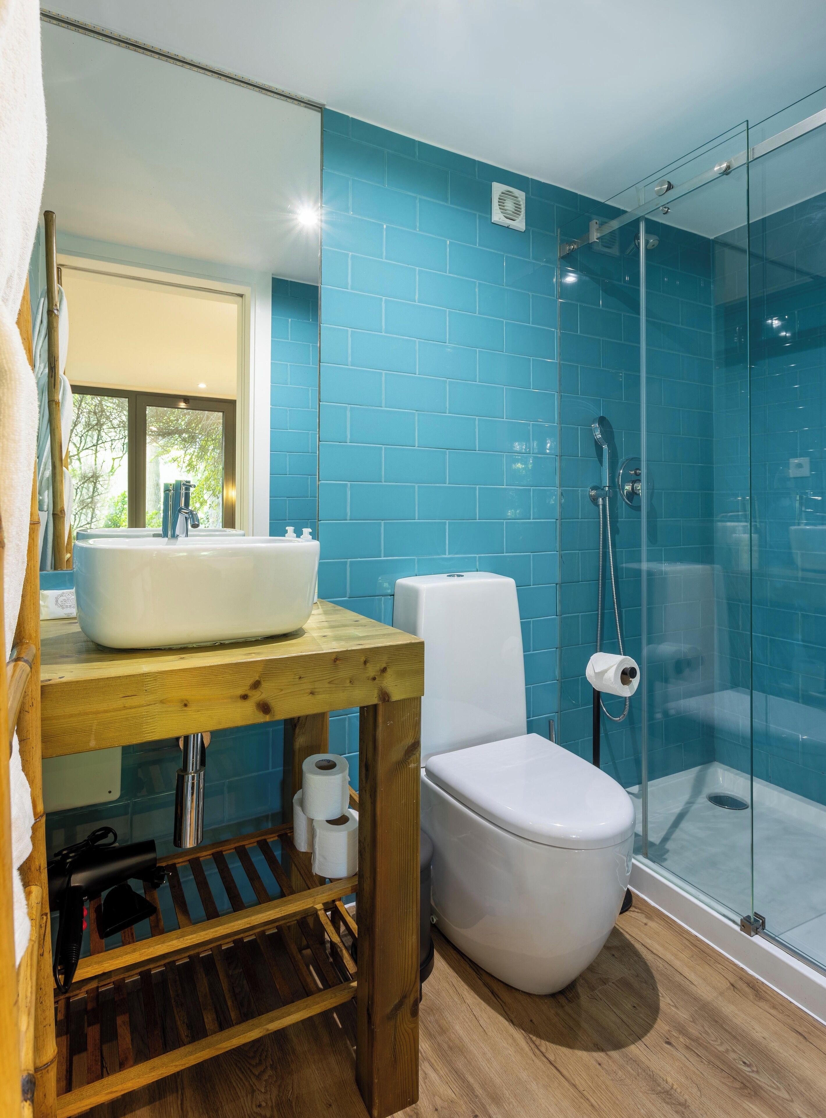 A bathroom with a wooden vanity, a white sink, a toilet, and a glass-enclosed shower.