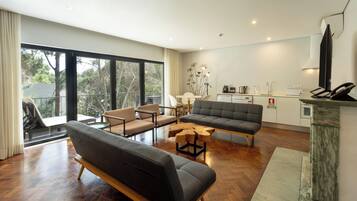 Uma sala de estar moderna com sofá, poltronas, mesa de centro e espaço de jantar. Inclui uma cozinha com eletrodomésticos e uma varanda com vista para árvores.