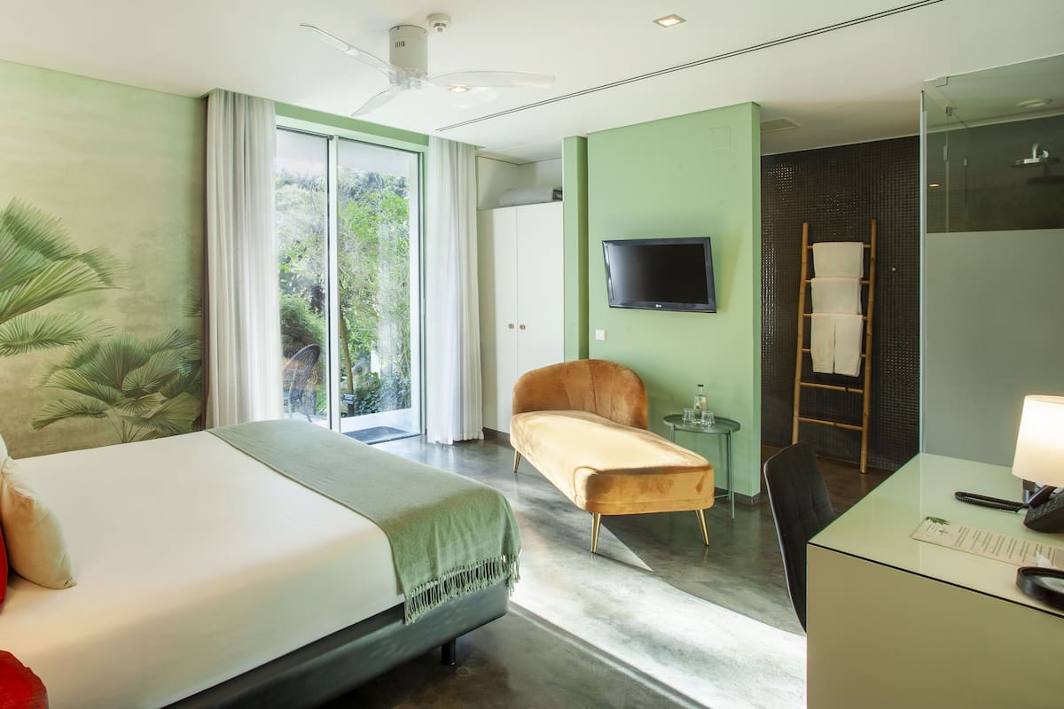 Habitación de hotel con cama, escritorio, silla, televisor y vistas a la vegetación por la ventana.