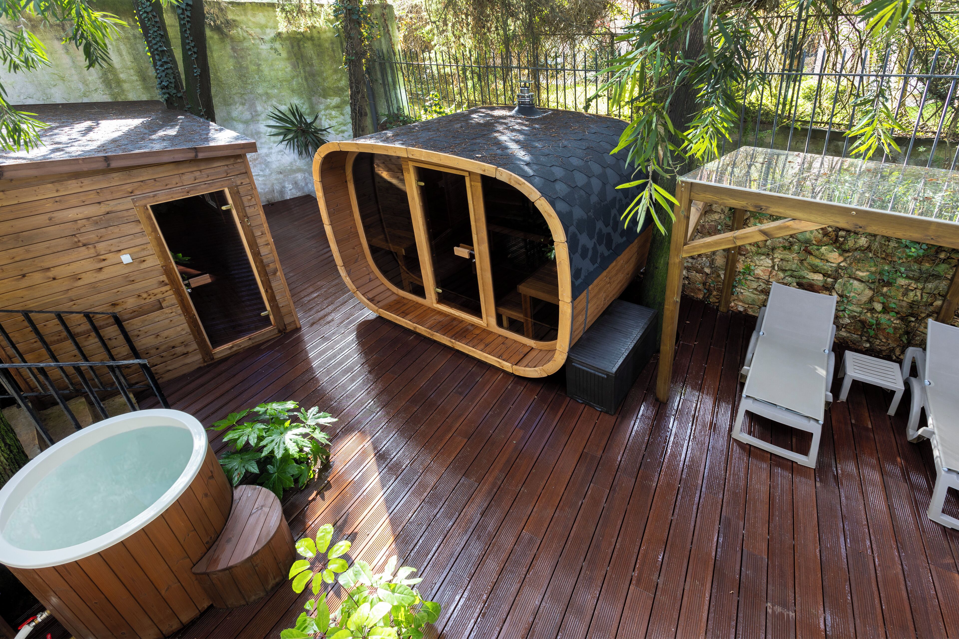 Un terrazzo in legno con vasca idromassaggio, una casetta gioco in legno e una zona relax con amaca.