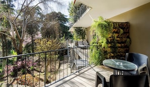 Ein Balkon mit Tisch und Stühlen, umgeben von Pflanzen und Bäumen.