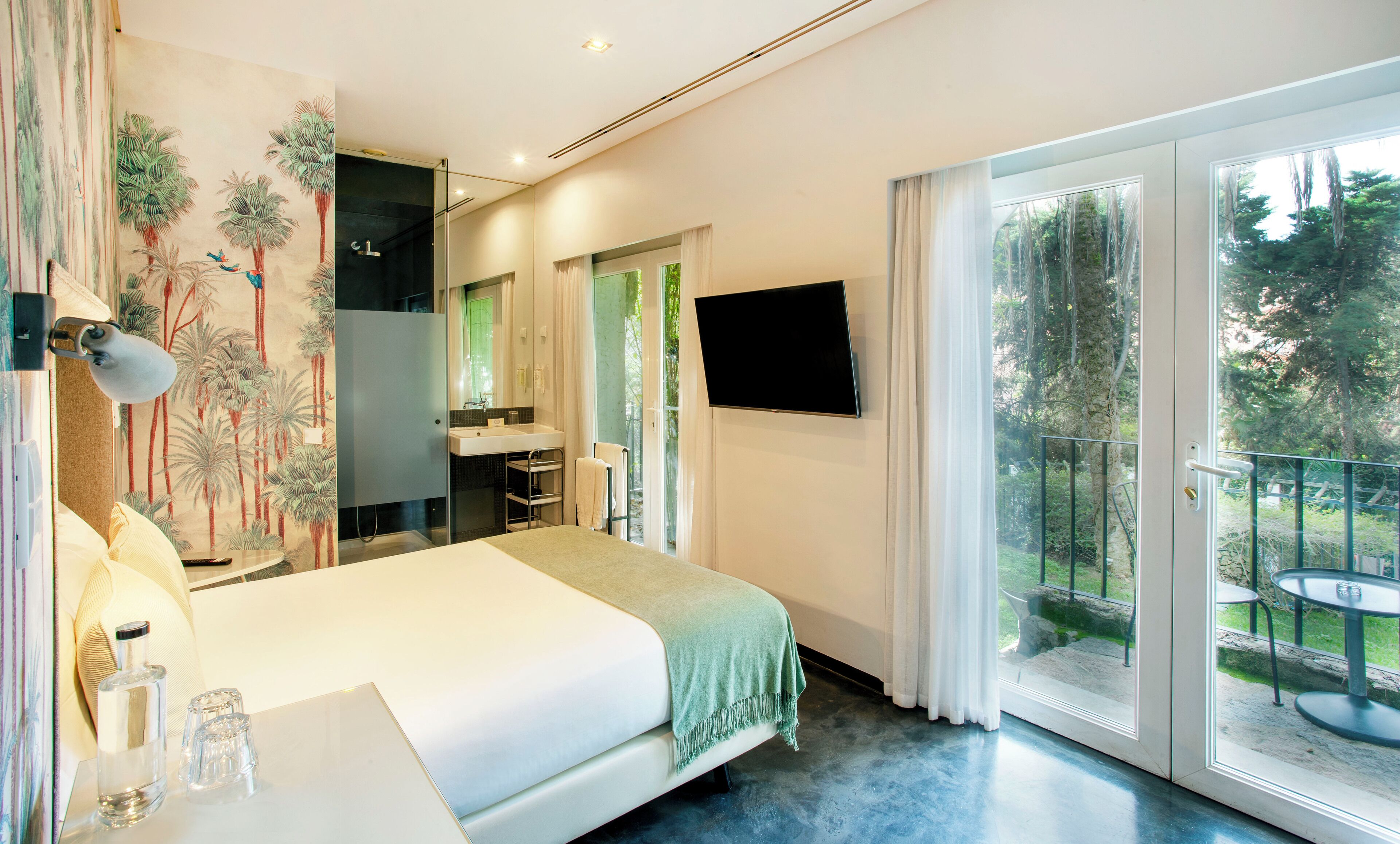 A bedroom with a bed, a bathroom, a TV, and a balcony with outdoor furniture.