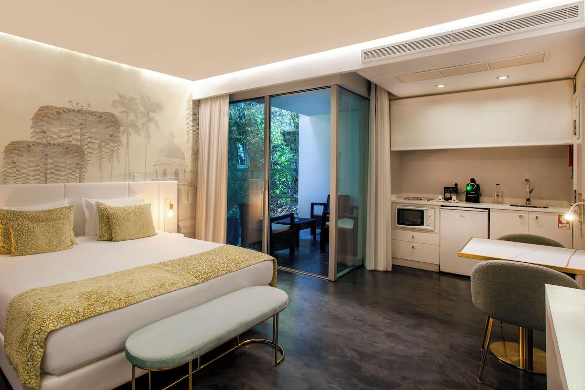 Una habitación de hotel moderna con una cama grande, un banco, un escritorio y una kitchenette.