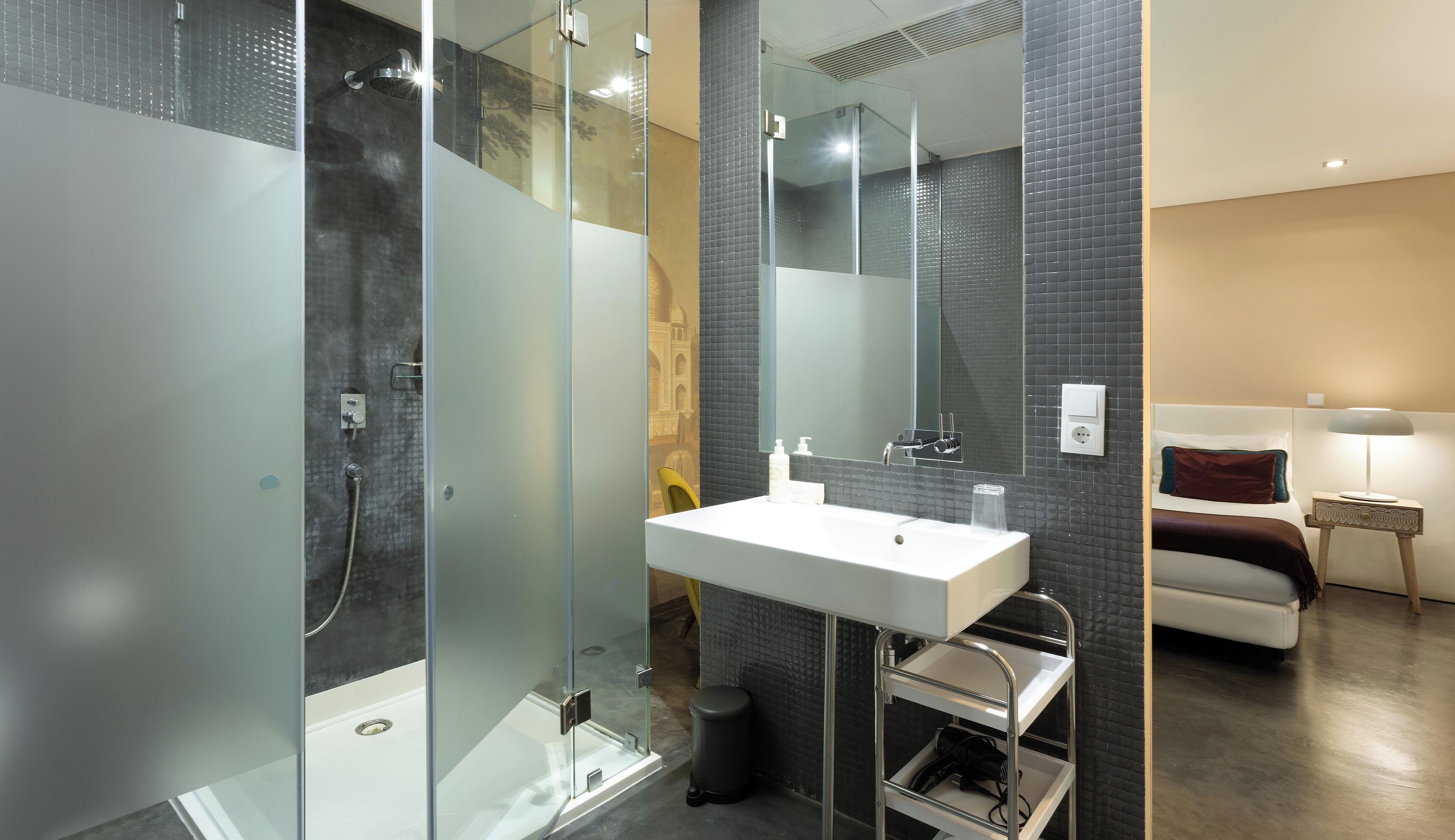 Un baño moderno con ducha envuelta en vidrio, lavamanos blanco y espejo.