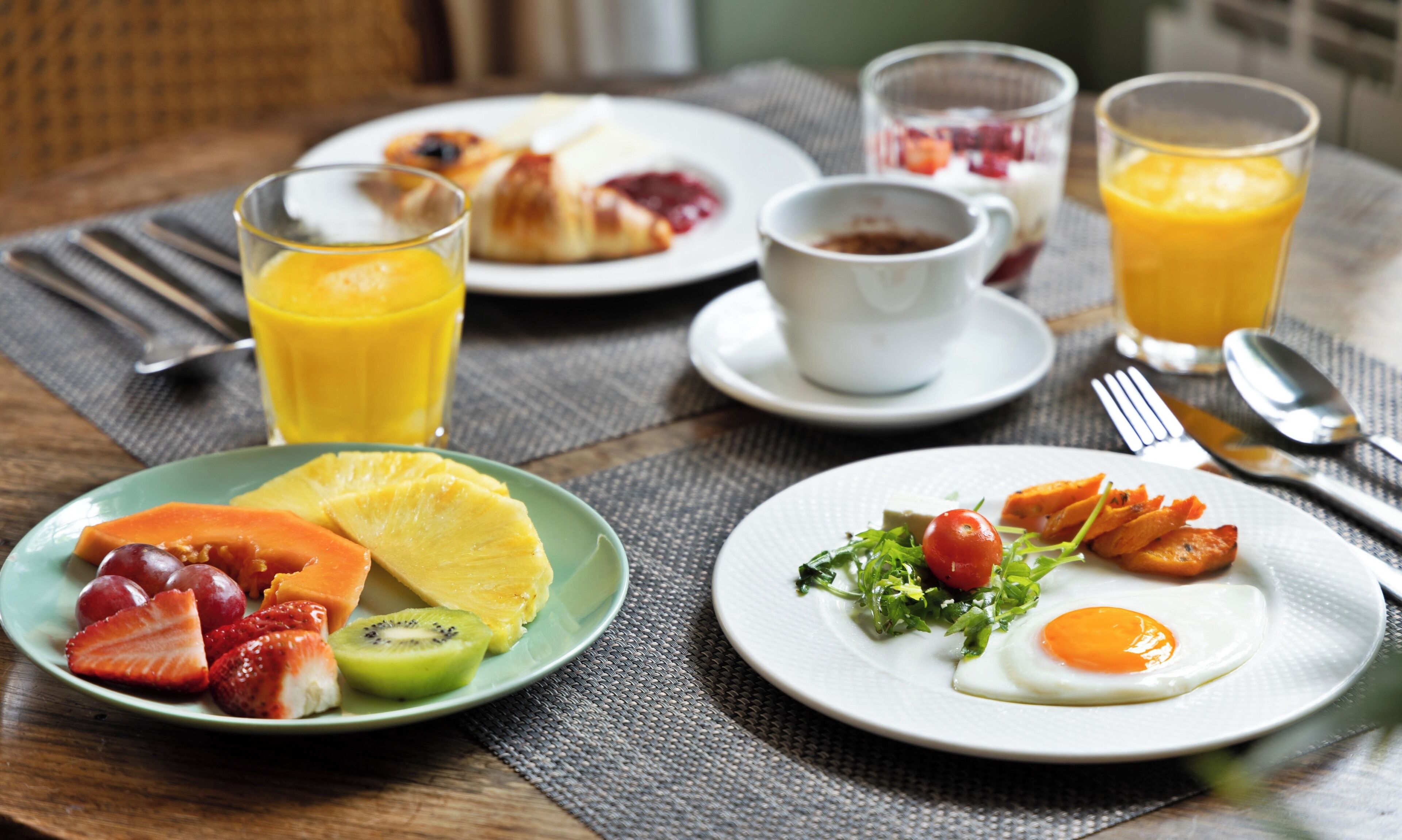 A breakfast table with plates of fruit, eggs, and pastries, along with glasses of orange juice.