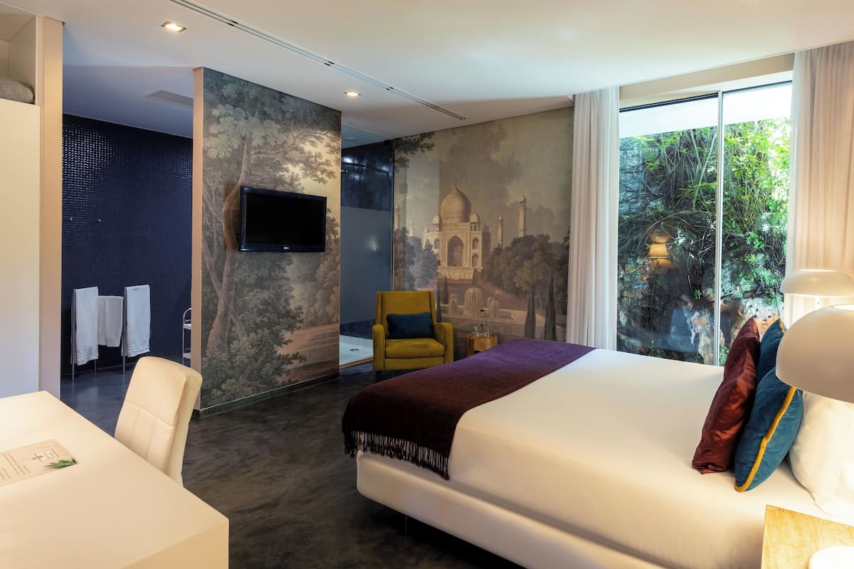 Habitación de hotel con una cama grande, una silla, un televisor y vista a zonas verdes.