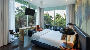 Habitación de hotel moderna con una cama grande, un escritorio y una silla. Hay un televisor montado en la pared y una ventana con vistas a zonas verdes.