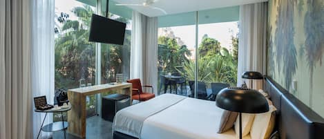 Habitación de hotel moderna con una cama grande, un escritorio y una silla. Hay un televisor montado en la pared y una ventana con vistas a zonas verdes.