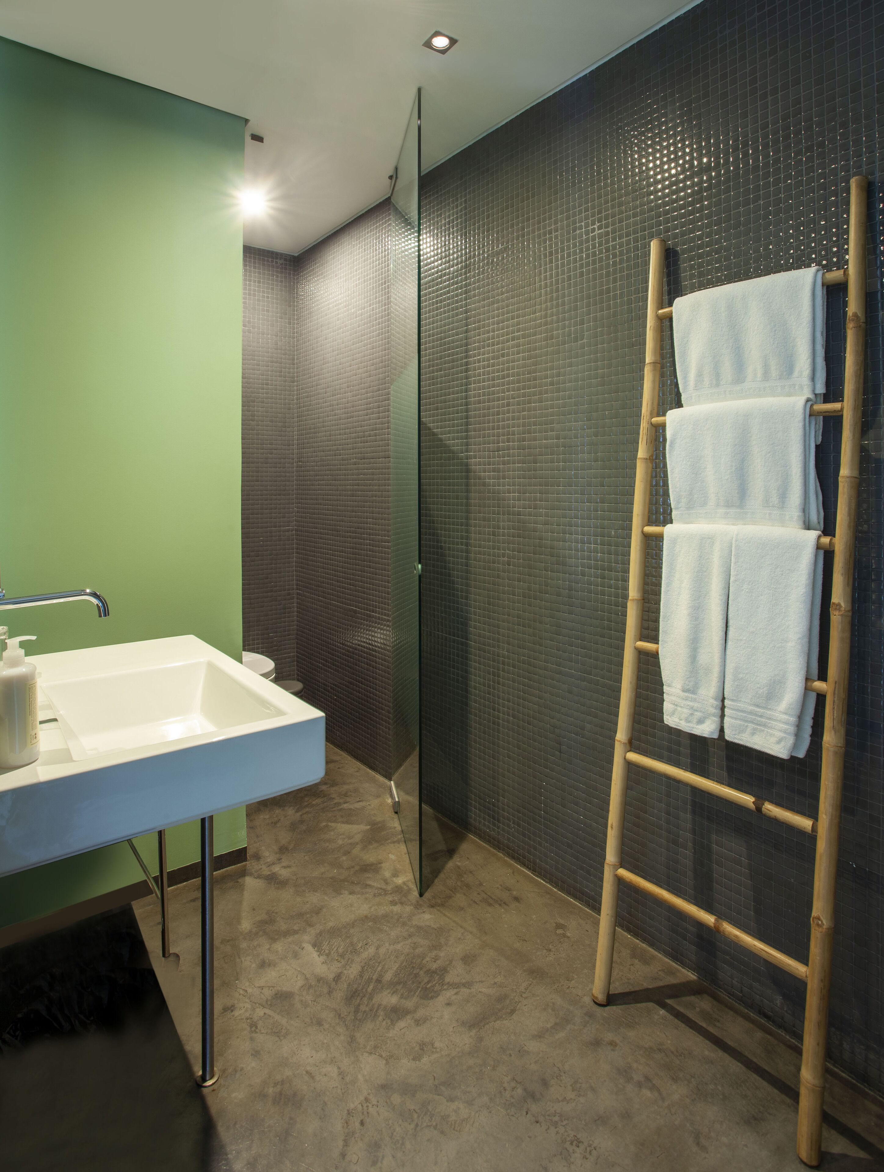 A bathroom with a white sink, a glass shower enclosure, and a bamboo towel rack with towels.