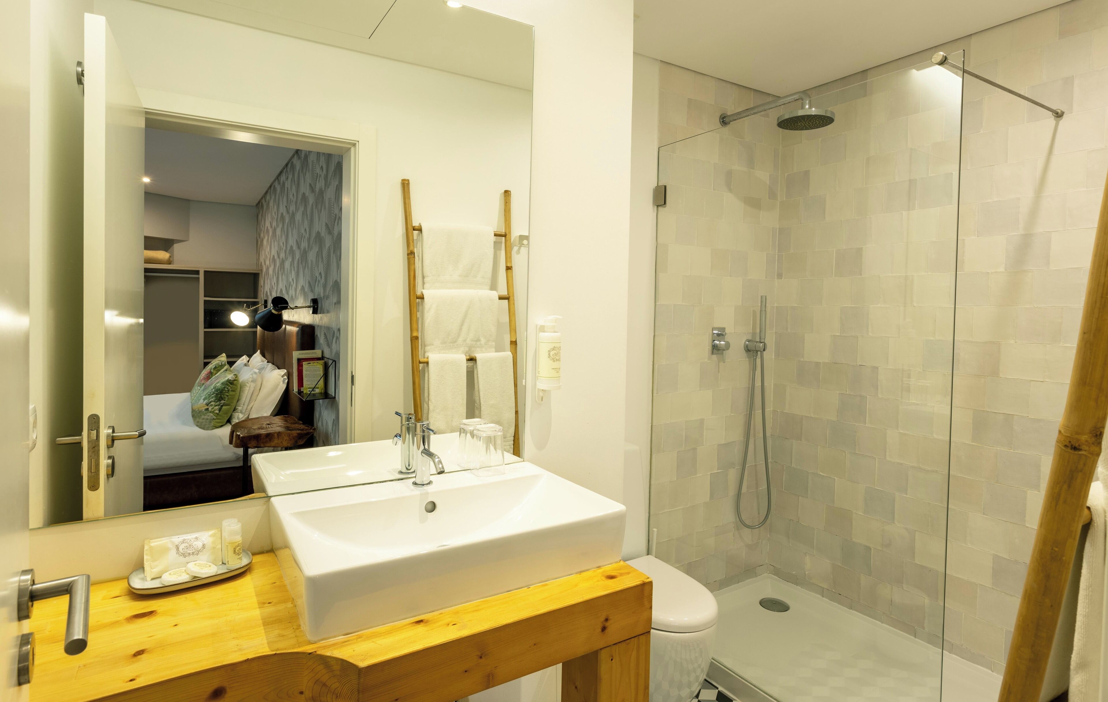 A modern bathroom with a double sink, a mirror, a shower, and a wooden bench.