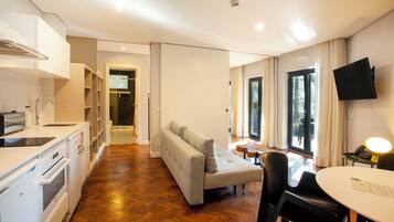 A modern kitchen with built-in appliances, a dining area with a round table, a sofa, and a TV mounted on the wall.