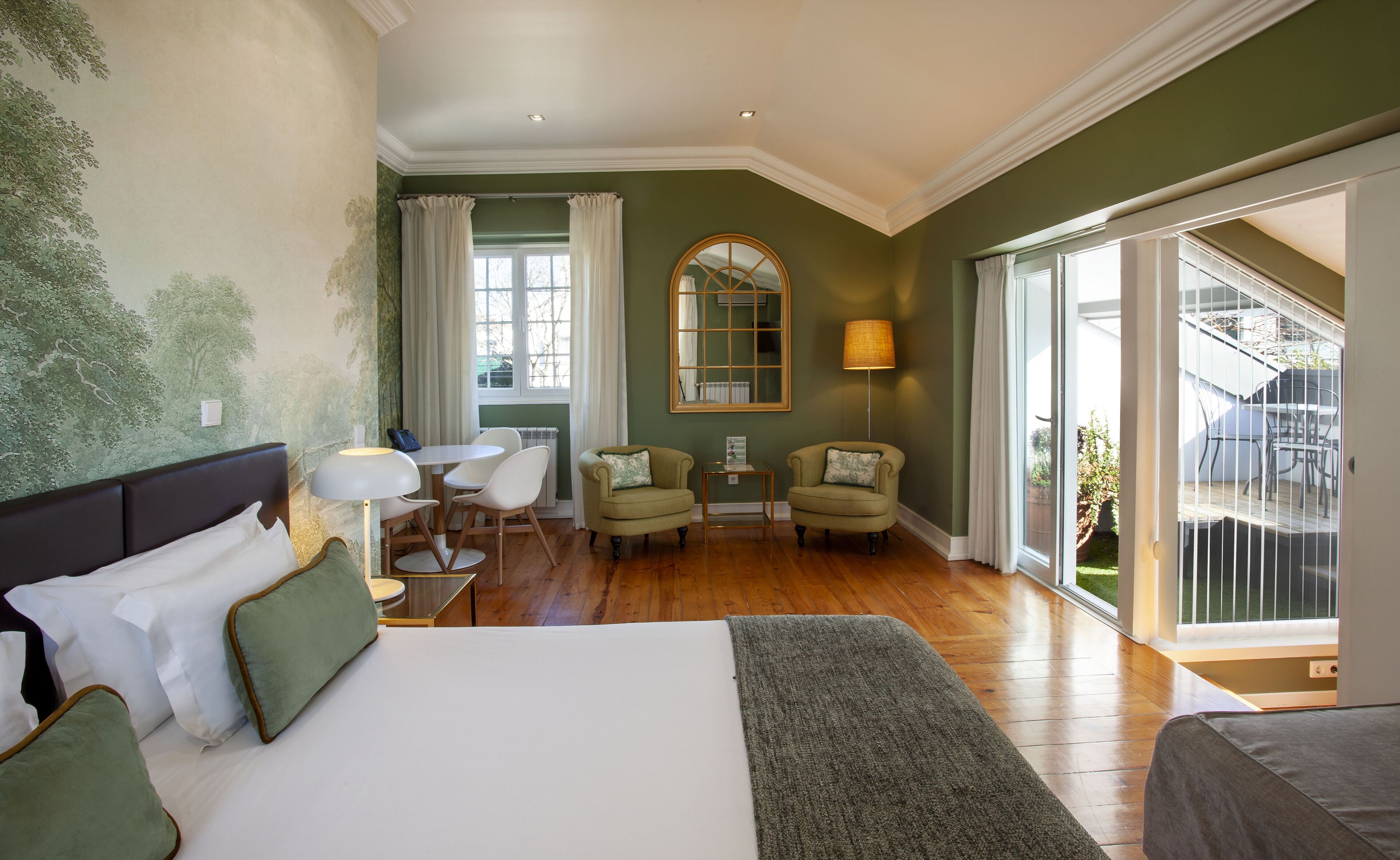 A hotel room with a large bed, two armchairs, a small table, a lamp, and a view of the outdoors.