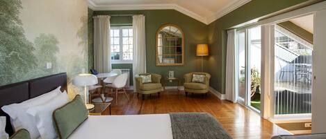 A hotel room with a large bed, two armchairs, a small table, a lamp, and a view of the outdoors.