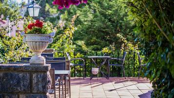 Un patio jardín con mesas y sillas de piedra, una urna decorativa con flores y un farol.