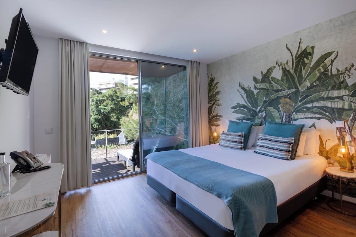 Una habitación de hotel moderna con una cama grande, un escritorio con teléfono y un puerta de vidrio que da a un espacio al aire libre.