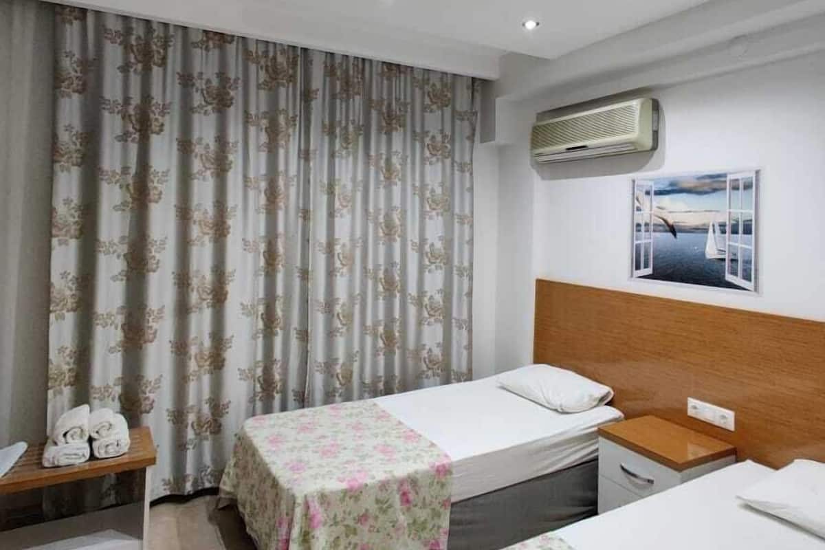 A hotel room with two beds, a wooden headboard, a small table with towels, and an air conditioning unit on the wall.
