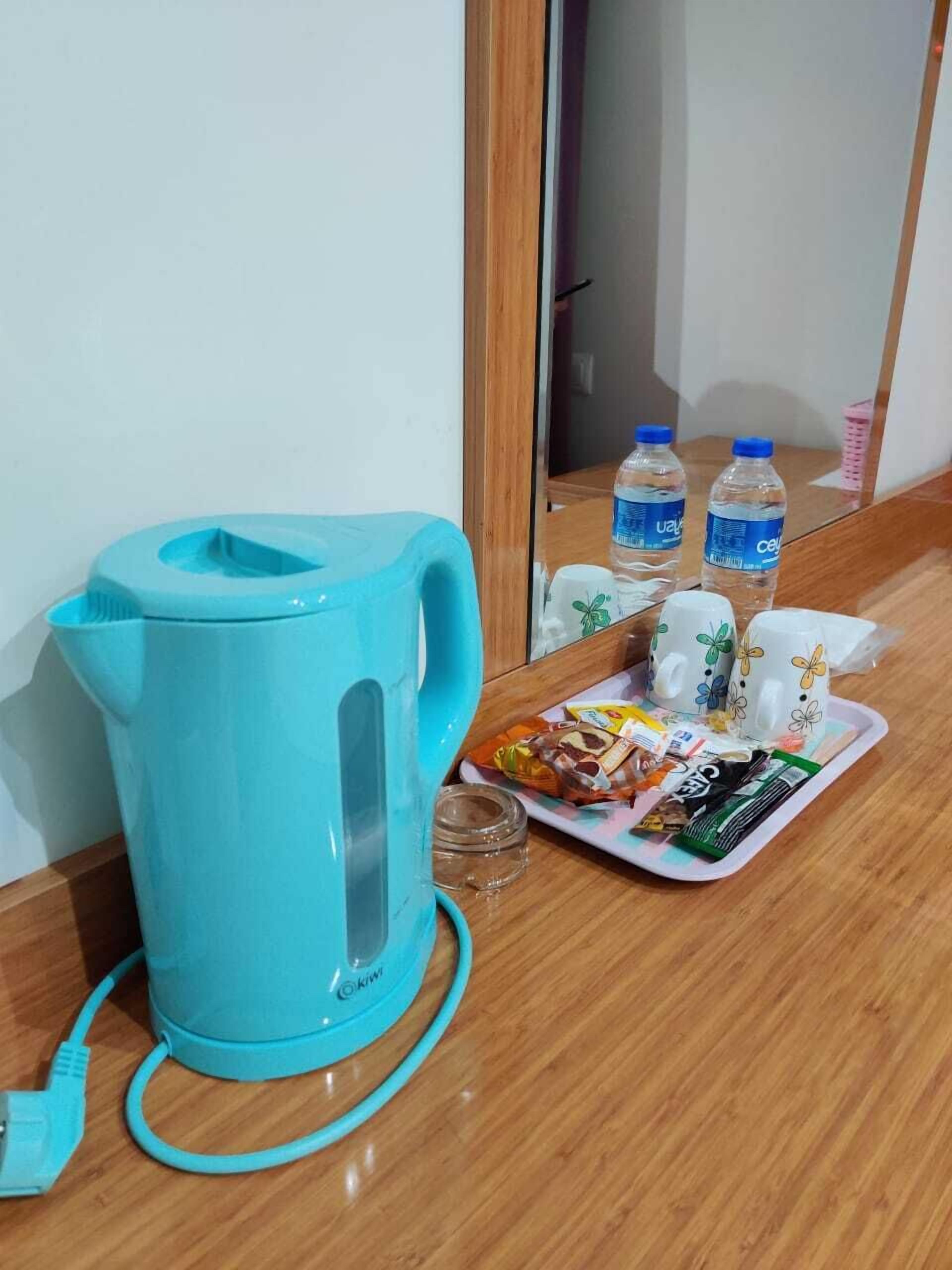 Una tetera eléctrica color turquesa sobre una mesa de madera con una bandeja de aperitivos y botellas de agua.