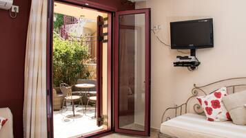 A bedroom with a bed, a TV mounted on the wall, and a sliding glass door leading to an outdoor patio with a table and chairs.