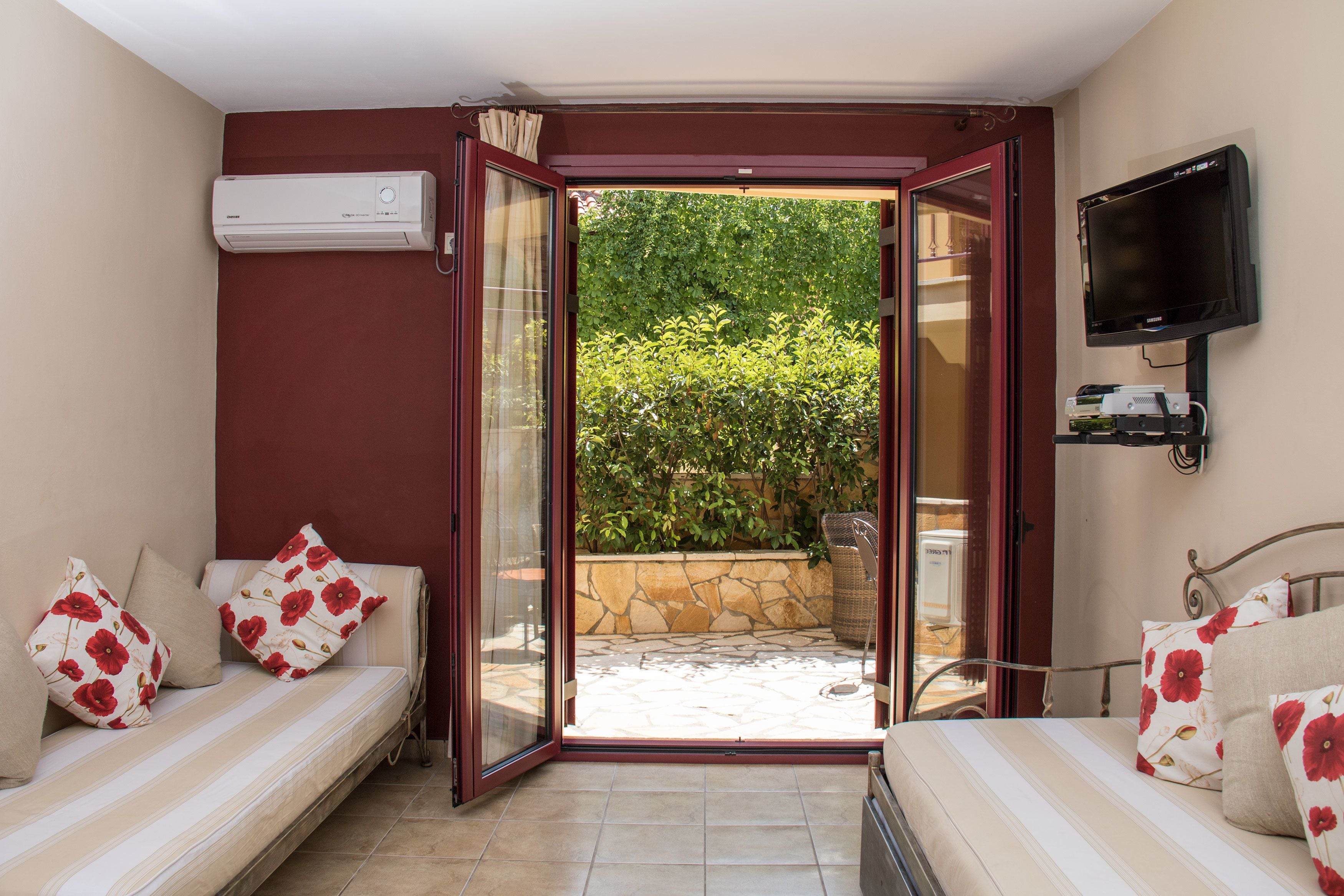 Una stanza con un letto, un divano, un condizionatore d'aria, una televisione e vista su un giardino attraverso una porta aperta.