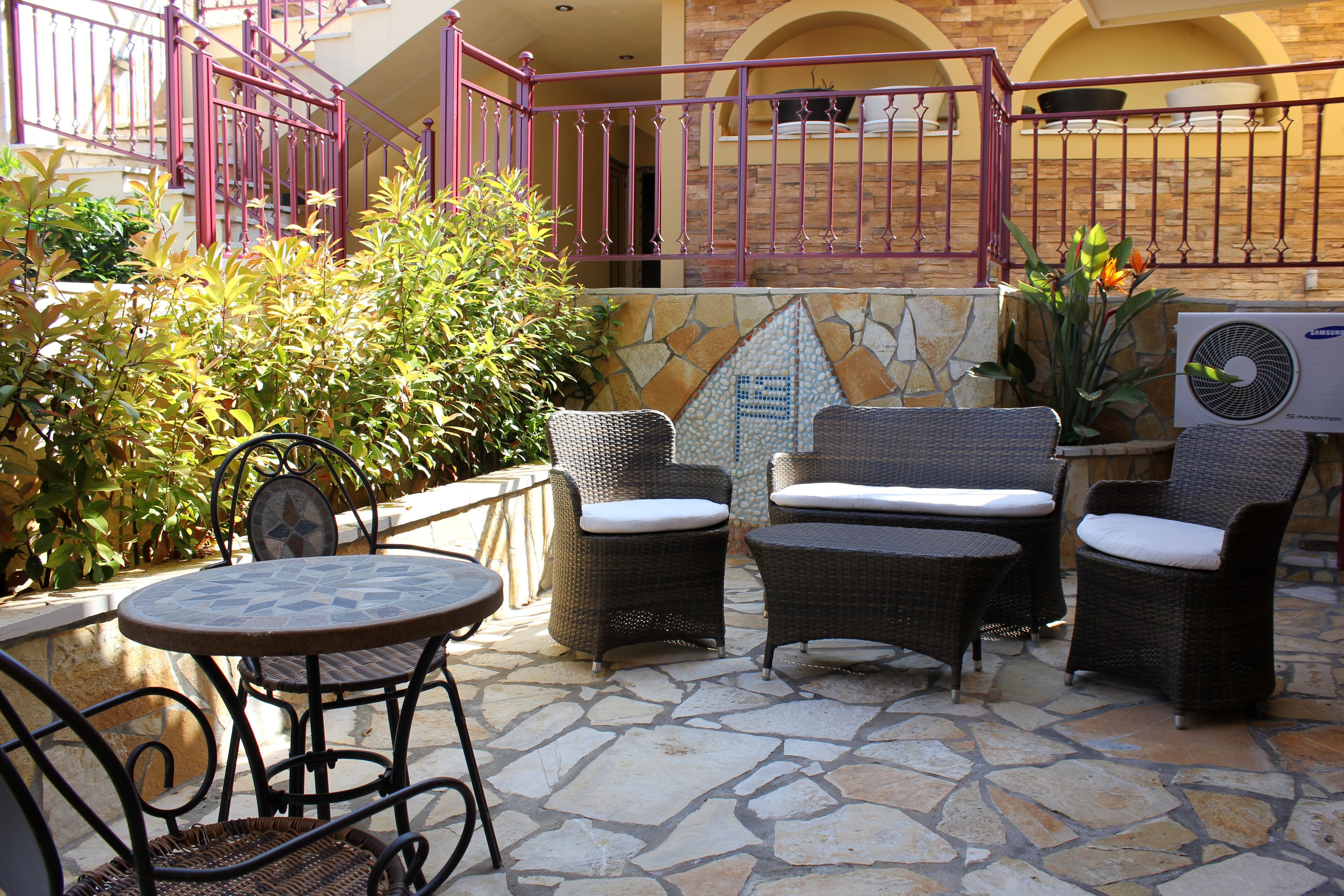 Un patio exterior con mobiliario de mimbre, suelo de piedra y vista a un edificio con balcón.