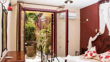 Un dormitorio con cama, escritorio y silla. Hay una puerta que da a un espacio exterior con plantas y una escalera.