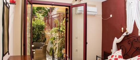 A bedroom with a bed, a desk, and a chair. There is a door leading to an outdoor area with plants and a staircase.