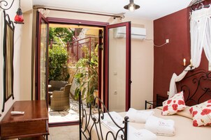 Un dormitorio con cama, escritorio y silla. Hay una puerta que da a un espacio exterior con plantas y una escalera.