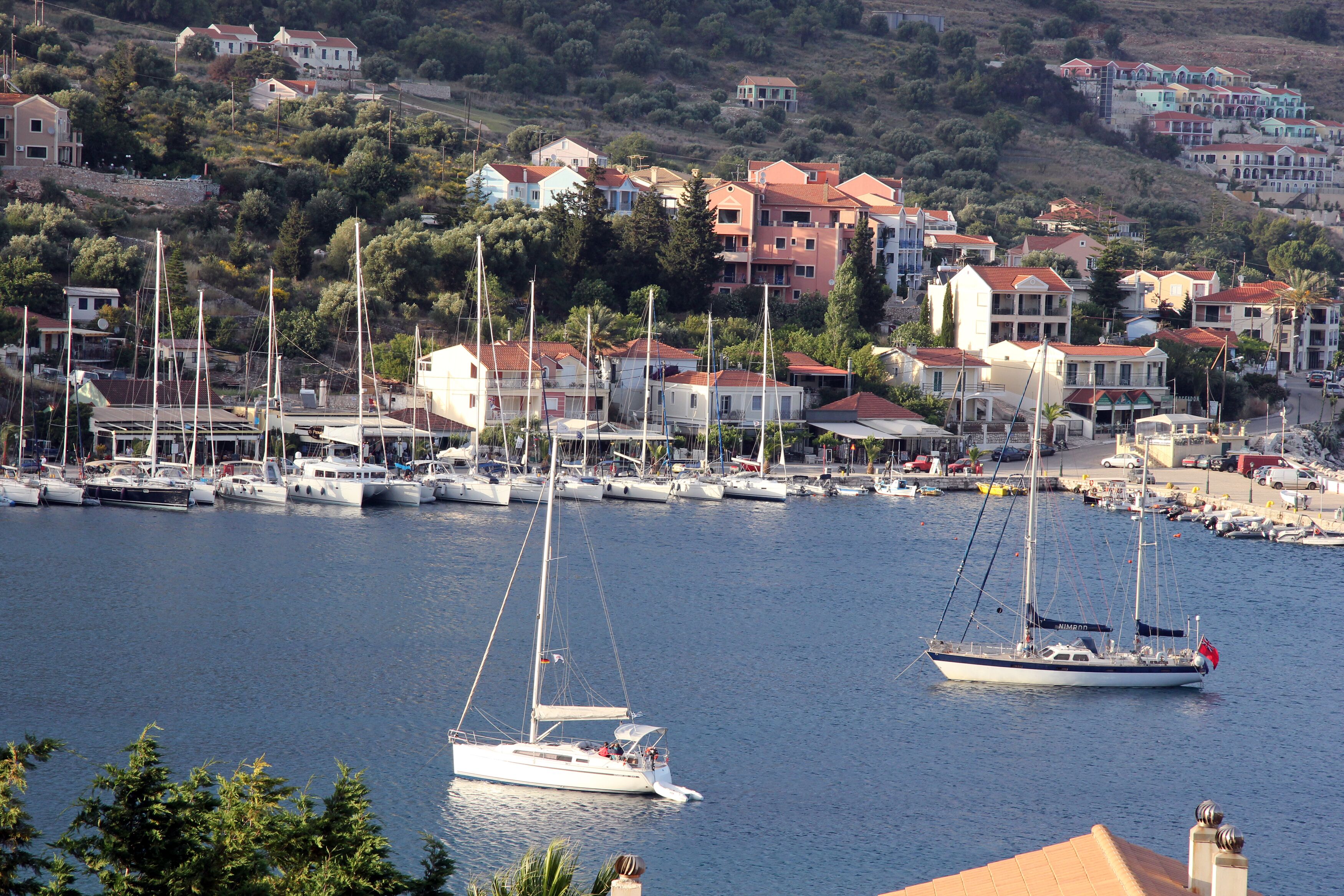 A marina with multiple sailboats docked, surrounded by residential buildings with red roofs.