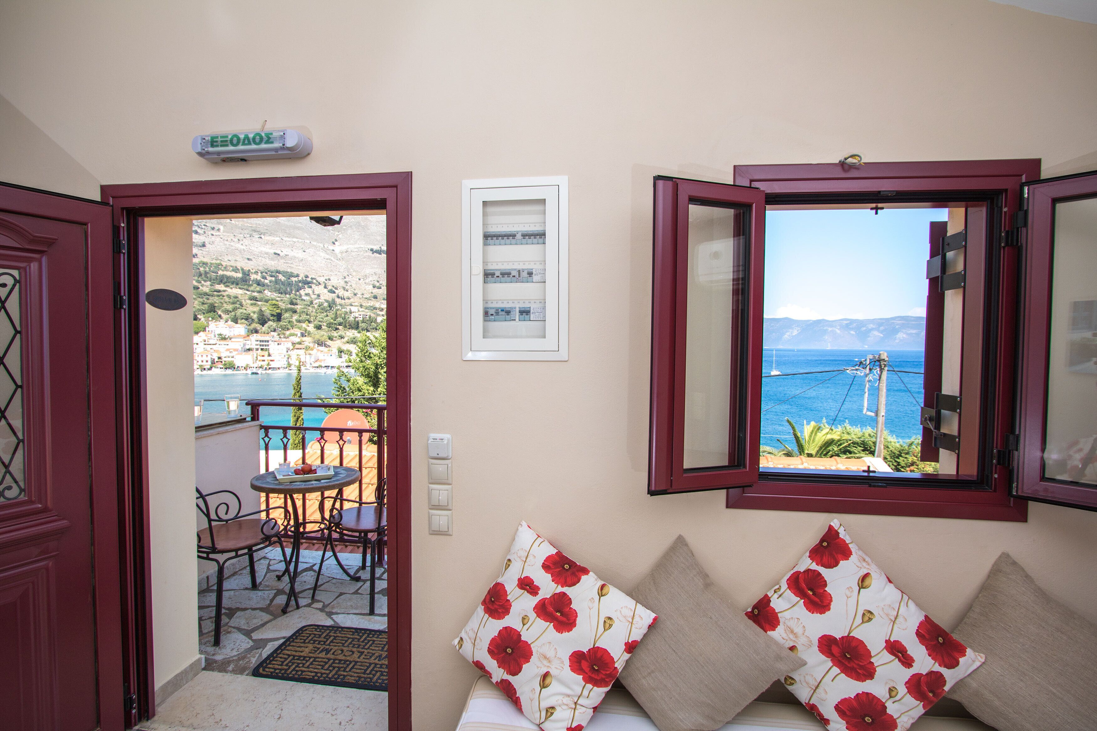 A room with a view of the sea, a balcony with chairs, and a door leading outside.