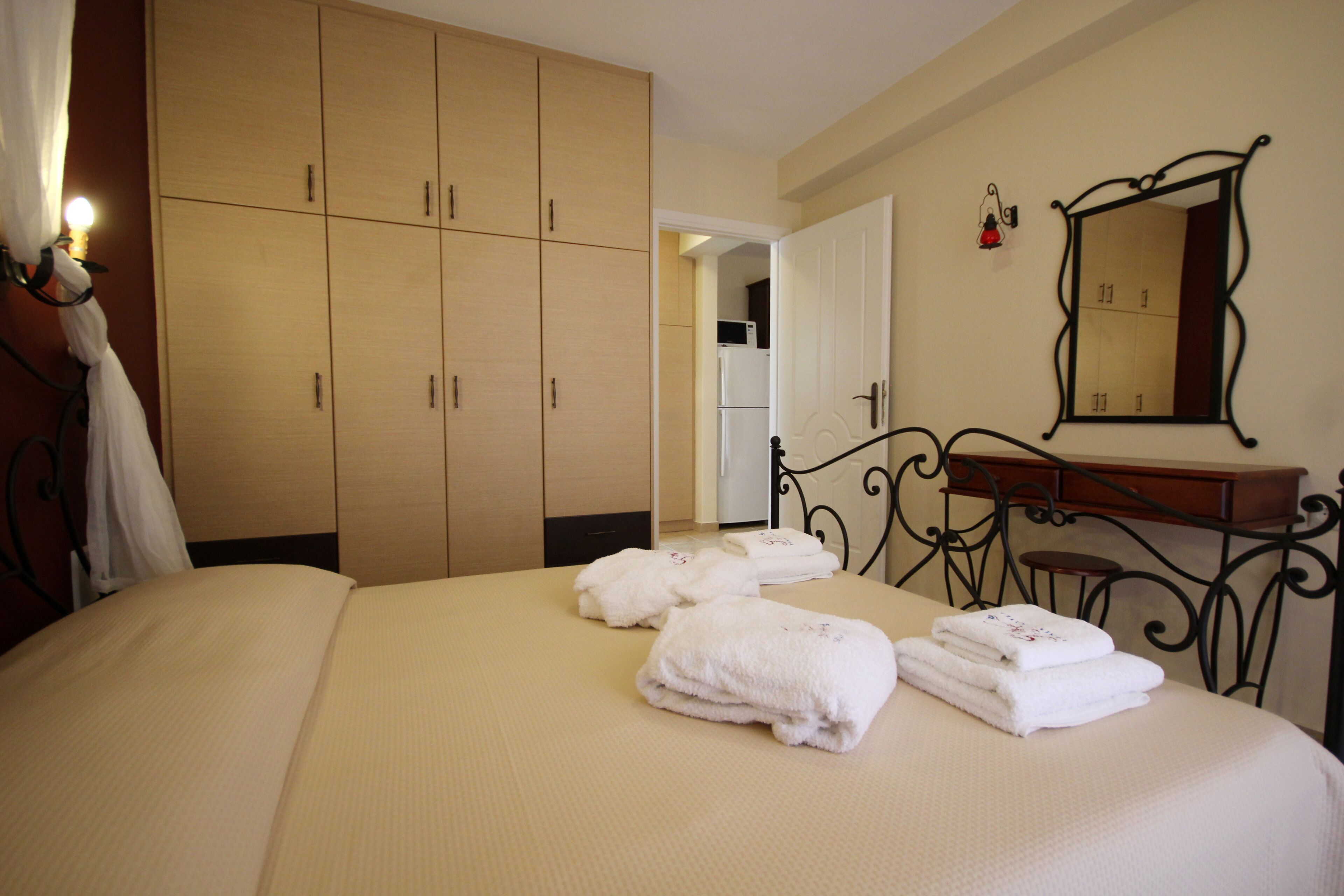 A hotel room with a bed, a wardrobe, a vanity with a mirror, and a door leading to a kitchen.